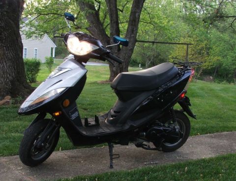 2008 Yamaha Zuma - A black scooter with a silver front panel is parked on a concrete path outdoors.