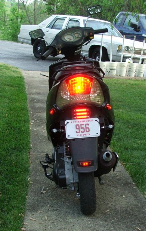 2008 Yamaha Zuma - A black scooter is parked on a sidewalk, with two cars visible behind it.