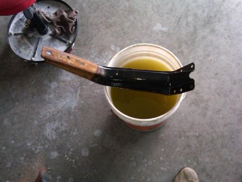 1986 Ford Bronco - Metal bracket being dipped into a bucket of fluid for cleaning or treatment.