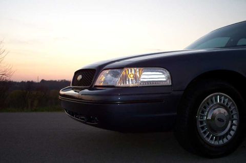 1998 Ford Crown Victoria - Close-up 3/4 front view of a dark blue Ford Crown Victoria sedan at dusk, showing the driver-side headlight assembly, chrome-trimmed grille…