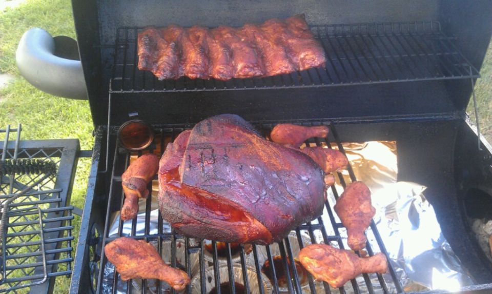 Smoker grill with ribs on top rack and a large cut of meat with chicken legs on bottom rack