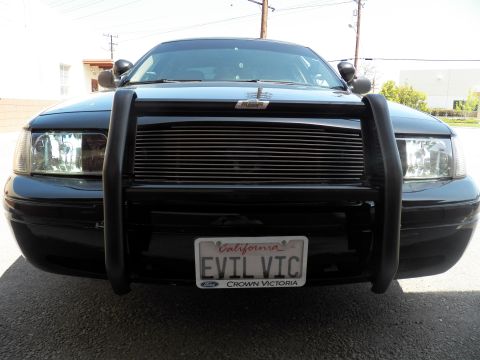 2003 Ford Crown Victoria - Direct front view of dark Ford sedan, push bar framing billet grille above EVIL VIC tag