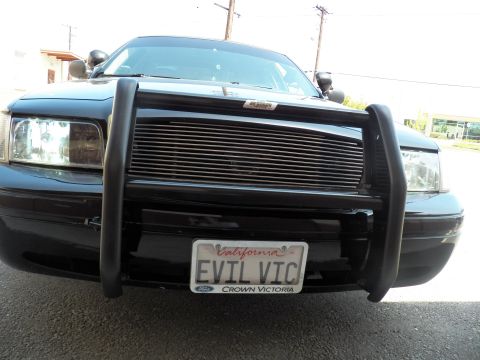 2003 Ford Crown Victoria - Black Ford sedan photographed low and close, brush guard and EVIL VIC California tag visible