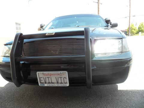 2003 Ford Crown Victoria - Angled front of dark Ford sedan, brush guard and billet grille with lit headlamp, EVIL VIC tag
