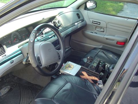 1999 Ford Crown Victoria - The interior of a 1999 Ford Crown Victoria police car is visible, equipped with police radio and other law enforcement gear.