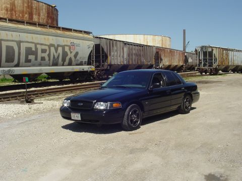 1999 Ford Crown Victoria - A black Ford Crown Victoria is parked on a gravel lot next to a train.