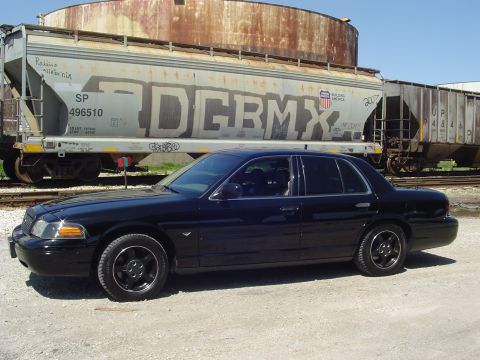 1999 Ford Crown Victoria - A black sedan is parked on a gravel lot with a train car in the background.