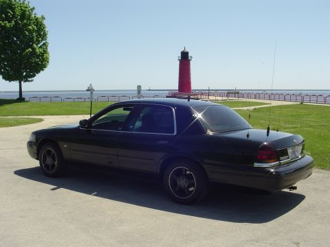 1999 Ford Crown Victoria - Black sedan parked near a lighthouse and the water on a sunny day.