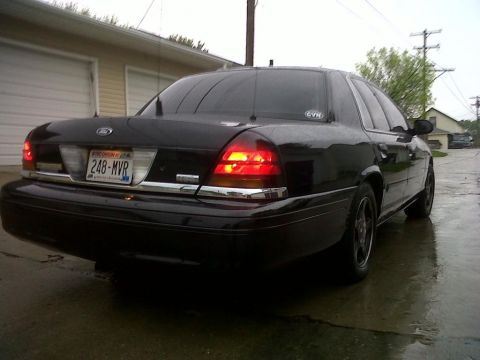 1999 Ford Crown Victoria - Rear view of a black Ford Crown Victoria parked on a wet surface, showing its taillights and license plate.