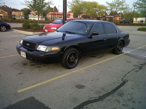 1999 Ford Crown Victoria - This black sedan, likely a 2003 model, is parked in a lot with other vehicles visible in the background.