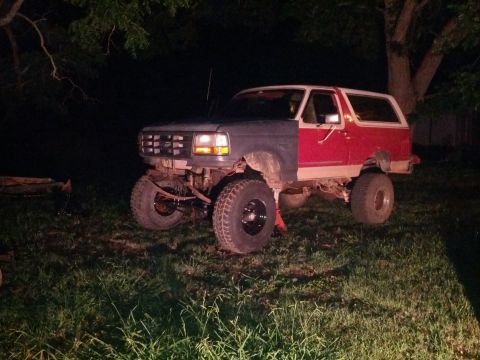1987 Ford Bronco - This 1987 Ford Bronco is partially disassembled and lifted on jack stands outdoors at night.