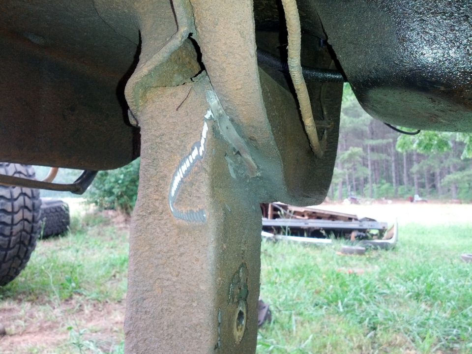 Close-up of rusty, modified vehicle frame with visible welds and a large tire in the background