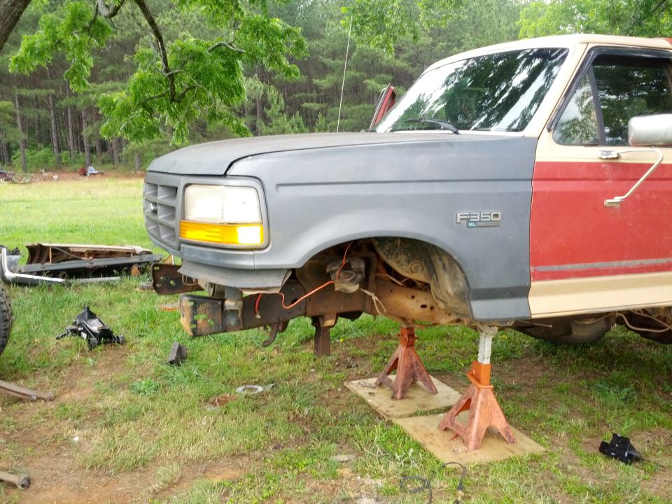 Ford F-350 truck with mismatched front fenders, raised on jack stands, with red and tan doors