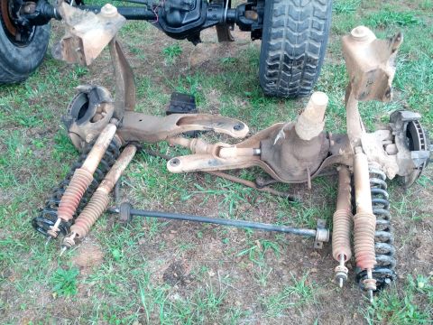 1987 Ford Bronco - Vehicle axle assemblies, shocks, and springs are disassembled and placed on the ground.