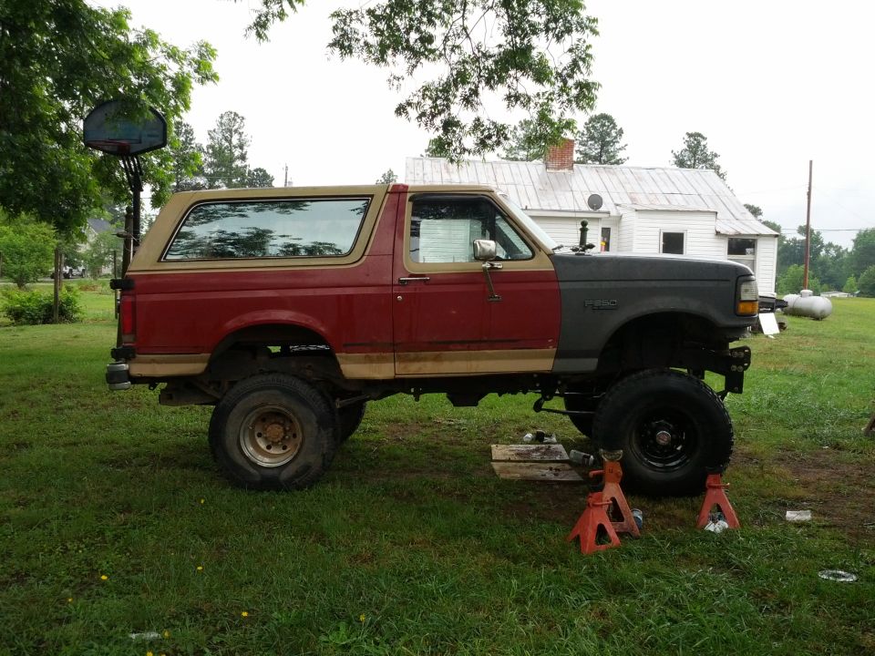 1987 Ford Bronco with red rear and gray front sections, lifted on jack stands