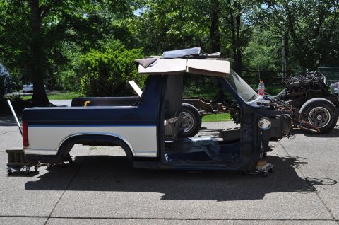 1986 Ford Bronco - Stripped 1986 Ford Bronco body being prepped for restoration, engine visible in background.