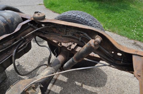 1986 Ford Bronco - Close-up of a heavily rusted vehicle frame, showing the rear axle and suspension components.