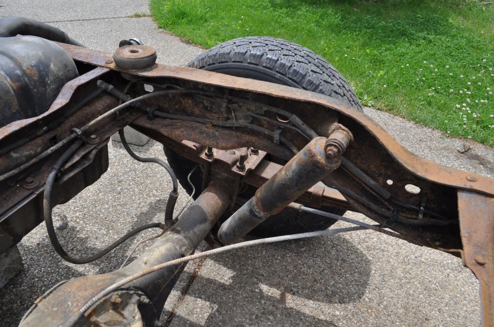 Rusted frame section with rear axle, shocks, and fuel tank. Tire visible