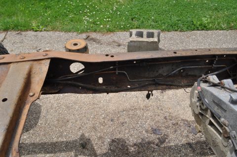 1986 Ford Bronco - The frame of a vehicle sits on a concrete surface, showing signs of rust and wear.