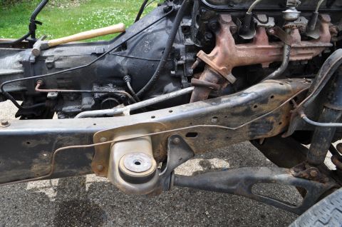 1986 Ford Bronco - Vehicle frame and engine components, including transmission and exhaust manifold, with a hammer on top.