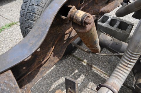 1986 Ford Bronco - This image shows the heavily rusted frame and suspension of a vehicle, with a tire visible in the background.