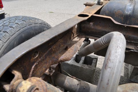 1986 Ford Bronco - Close-up view of a heavily rusted vehicle frame and exhaust system, with a tire visible on the left.
