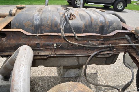 1986 Ford Bronco - The fuel tank and frame components are visible, with significant rust and fuel lines attached.