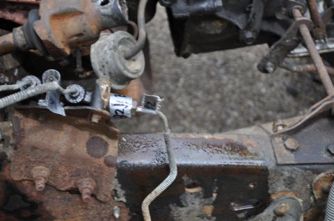 1986 Ford Bronco - Close-up view of aged vehicle undercarriage components, including a brake line and wiring.