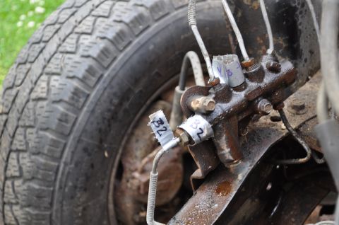 1986 Ford Bronco - Brake master cylinder assembly with labeled lines, adjacent to a vehicle tire.