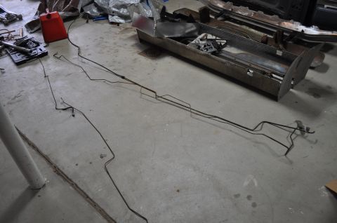1986 Ford Bronco - Various metal brake lines and chassis components are spread out on a garage floor.