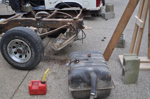 1986 Ford Bronco - A heavily rusted vehicle frame and suspension components are visible, alongside a detached fuel tank and a red gas can.