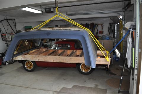 1986 Ford Bronco - Car body and camper shell suspended by straps in a garage during a teardown process.