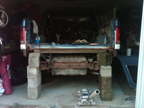 1986 Ford Bronco - The rear of a pickup truck is shown with its bed removed and the chassis elevated on cinder blocks.