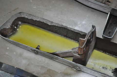1986 Ford Bronco - This metal part contains a yellow liquid and shows signs of rust and wear.