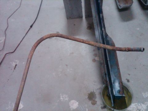 1986 Ford Bronco - A close-up view of a rusty metal tube and part of a vehicle frame resting on a concrete surface.