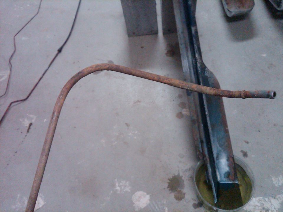 rusted metal tube bent over a dark frame piece on a concrete floor