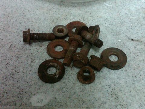 1986 Ford Bronco - A collection of corroded fasteners, including bolts and washers, are scattered on a textured surface.