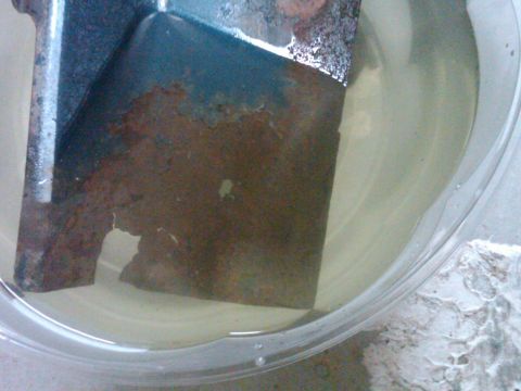 1986 Ford Bronco - A metal part with significant rust is submerged in a clear liquid, likely for rust removal.