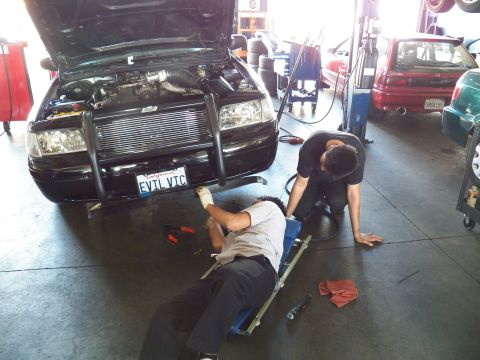 2003 Ford Crown Victoria - EVIL VIC Ford sedan being serviced, technician on creeper under bumper, second wiping floor