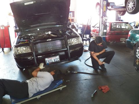 2003 Ford Crown Victoria - EVIL VIC Ford sedan under work, one tech on creeper and another crouched with an air hose