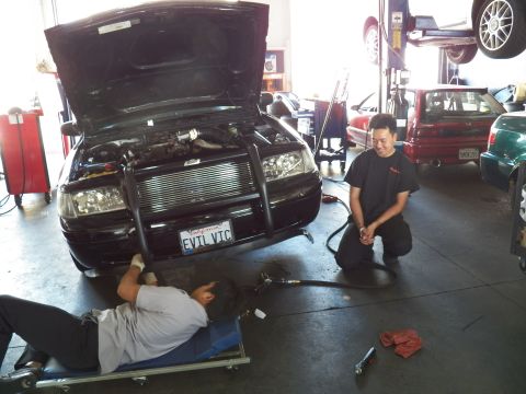 2003 Ford Crown Victoria - EVIL VIC Ford sedan being serviced as a kneeling tech smiles, another lies on a creeper