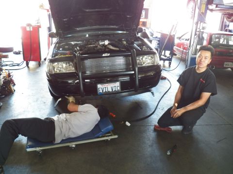 2003 Ford Crown Victoria - Mechanic in black shirt poses by the EVIL VIC Crown Victoria front end while a second worker lies underneath