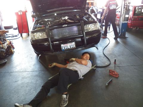 2003 Ford Crown Victoria - Worker rests on a creeper before the EVIL VIC Crown Vic front bumper with tools laid out on the shop floor