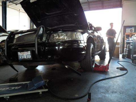 2003 Ford Crown Victoria - Mechanic stands next to the lifted EVIL VIC Crown Victoria, air hose running across the shop floor