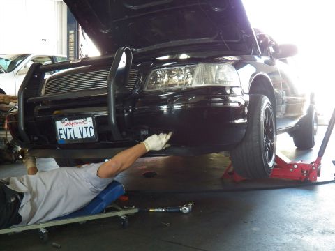 2003 Ford Crown Victoria - Gloved worker reaches under the EVIL VIC Crown Victoria bumper, torque wrench resting on the floor