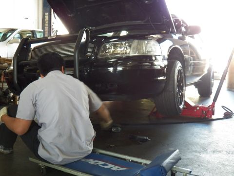 2003 Ford Crown Victoria - Mechanic crouches at the EVIL VIC Crown Victoria front end with the car raised on a floor jack