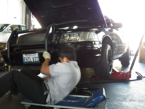 2003 Ford Crown Victoria - Worker reaches into the EVIL VIC Crown Victoria front bumper area, hood raised over the engine bay