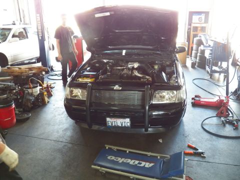 2003 Ford Crown Victoria - Open engine bay of the EVIL VIC Crown Victoria with a worker standing by tool benches in the shop