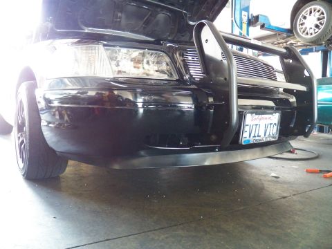 2003 Ford Crown Victoria - Low-angle shot of the EVIL VIC Crown Vic front bumper, wheel and brush bar with cars on lifts behind