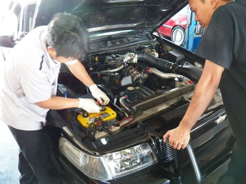 2003 Ford Crown Victoria - Mechanic works on a black sedan's engine compartment, lifting a battery with a yellow carrier strap.